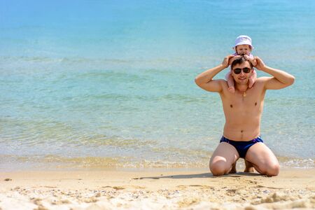 Young father in glasses sits on the beach with his daughterの写真素材
