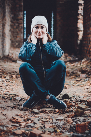 Photo of a young beautiful girl in ruins against a background of brick walls in a jacket and trousers. In the photo there is a cold toning.の写真素材