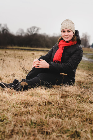 A beautiful girl sits in a field with a hat and a scarfの写真素材