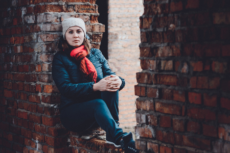 Beautiful young woman sits in ruins on an orange background in a cap and scarfの写真素材