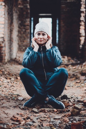Beautiful young woman sits in ruins on an orange background in a cap and scarfの写真素材