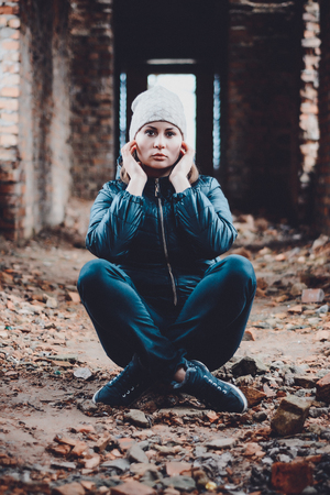 Beautiful young woman sits in ruins on an orange background in a cap and scarfの写真素材