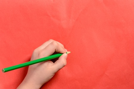A photo of the hands of a young boy holding pencils and pens on colored backgroundsの写真素材