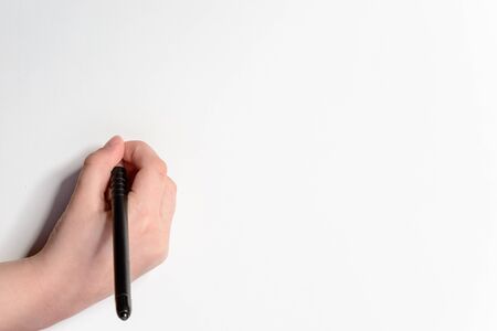A photo of the hands of a young boy holding pencils and pens on colored backgroundsの写真素材