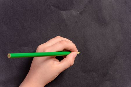 A photo of the hands of a young boy holding pencils and pens on colored backgroundsの写真素材
