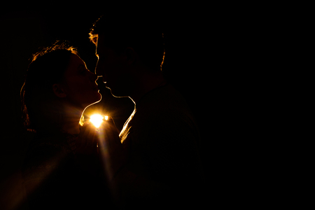 A pair of lovers is in the dark, through which the rays break through and illuminate their silhouetteの写真素材