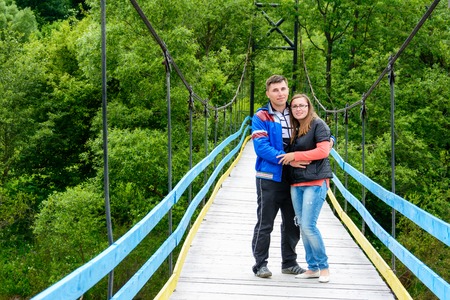 Young lovers are standing on a bridge over a river near green trees 2018の写真素材