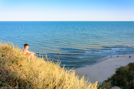 A young man in a red shirt sits on a hill in the background of the sea 2018の写真素材