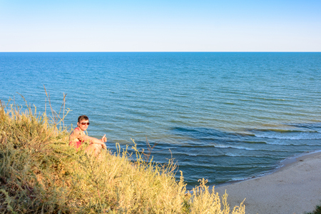 A young man in a red shirt sits on a hill in the background of the sea 2018の写真素材