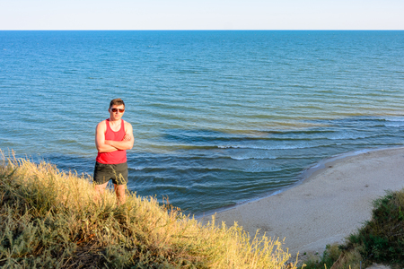 A young man in a red shirt sits on a hill in the background of the sea 2018の写真素材