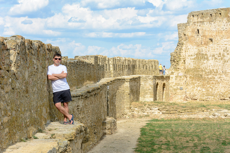 A young man in a white T-shirt and sunglasses stands on the wallの写真素材