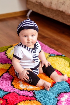 A pretty baby in a striped shirt and hats seated on the mat in the room 2018の写真素材