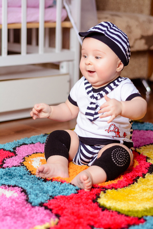 A pretty baby in a striped shirt and hats seated on the mat in the room 2018の写真素材