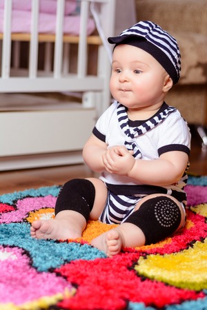 A pretty baby in a striped shirt and hats seated on the mat in the room 2018の写真素材