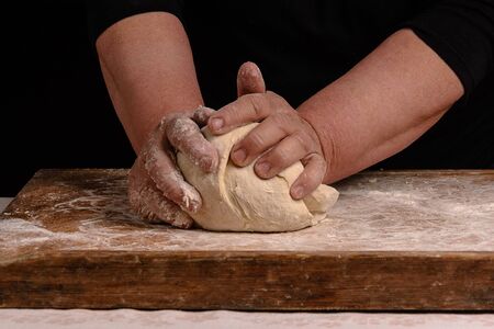 An old woman's grandmother is kneading a dough for the preparation of bread on a black background