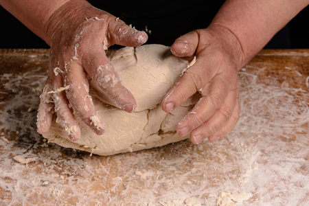 An old woman's grandmother is kneading a dough for the preparation of bread on a black backgroundの写真素材