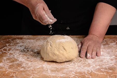 An old woman's grandmother is kneading a dough for the preparation of bread on a black backgroundの写真素材
