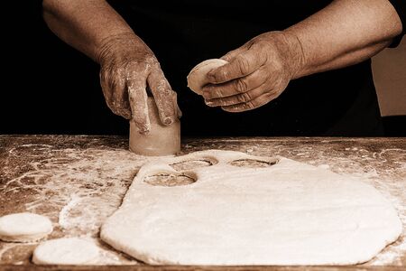 Granny squeezes a glass of a circle in a dough on the table 2018の写真素材