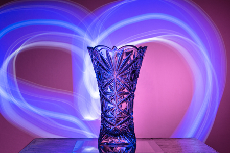 The crystal vase on a red background is illuminated with rays of the form of the heartの写真素材