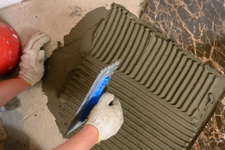 Close-up of a master's hand that makes furrows in a glutinous solution for laying marble tiles