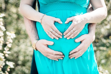 A man holds his arms in the form of a heart on the stomach of a pregnant woman in a blue dress