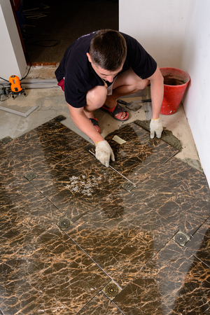 A man places a ceramic tile under pressure over a glue in room of brown colorの写真素材