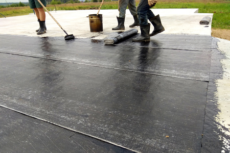 Roofer worker painting bitumen praimer at concrete surface by the roller brush Waterproofingの写真素材