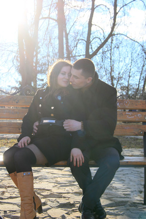 Beautiful happy young couple sitting on the bench in sunny park and making heart gesture together 2018の写真素材