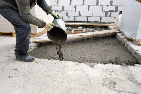 auxiliary worker pours out of a bucket liquid cement mortar on the floor between the floors of the houseの写真素材