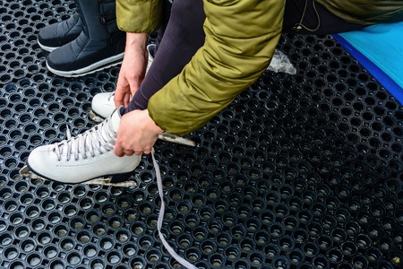 A young woman tied laces on white skates before riding a skating rinkの写真素材