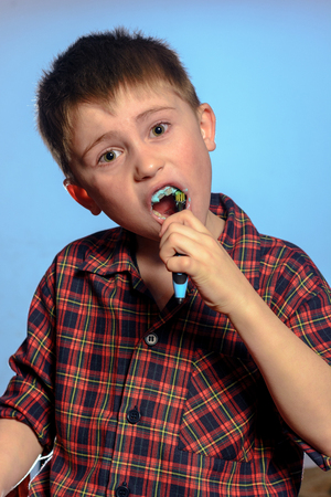 A cute boy in a pajamas brushes teeth with toothpaste before bedtime on a blue background 2019の写真素材