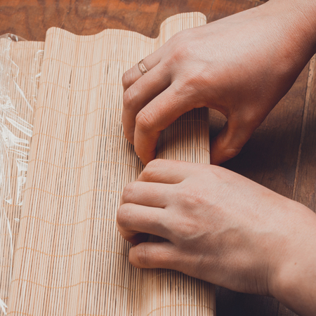 A female cook prepares sushi in the kitchen and wraps a letter to the nori in the roll 2019