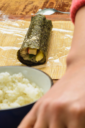 A female cook prepares sushi in the kitchen and wraps a letter to the nori in the roll 2019の写真素材