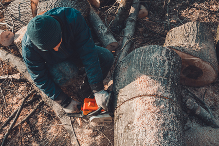 Harvesting firewood for winter, a man in glasses cut a tree by chainsaw holding it in his hands 2019の写真素材