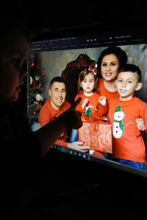 Los Angeles, California, USA - 22 December 2018: A little girl looks at her new year's family photo on the computer monitor in the Photoshop program 2019のeditorial素材