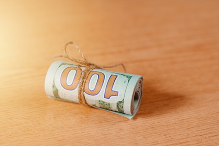 A roll of a hundred dollar bills on a light brown background. 2019の写真素材