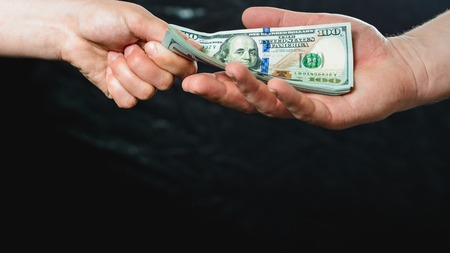 Close up of a businessman's hands holding money over a black background. 2019