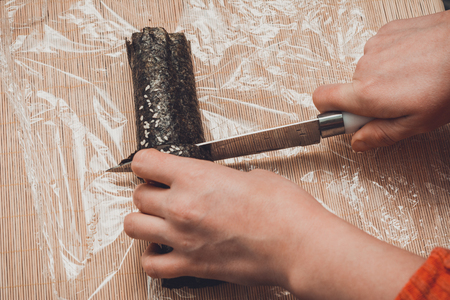 A woman in the kitchen cuts the knife with a roll of sushi at the level of the pieces for visitors 2019の写真素材