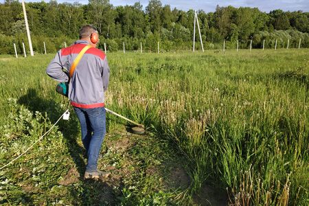 A man rows grass with an oak trimmer in the field, in the yard is summer and the sun shines. 2019