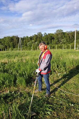 The headphone and glasses worker mows the grass in the field