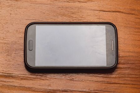 Small black smartphone lies on a wooden table. 2019