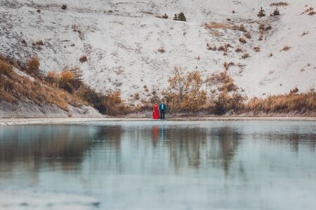 Beautiful couple walking in the phosphate-gypsum white mountains of Ukraine, the girl in a red dress on a background of a green lake. 2019の写真素材