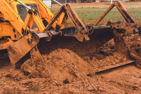 A close-up excavator loads soil into the bucket for further road installation. 2019の写真素材