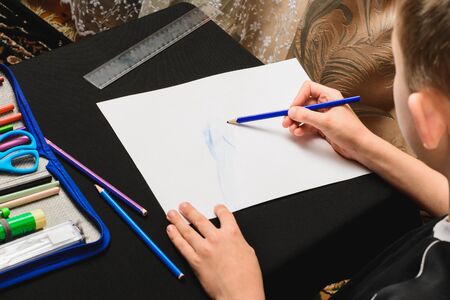 A boy sits at a table and draws pencils on white paper.2020の写真素材
