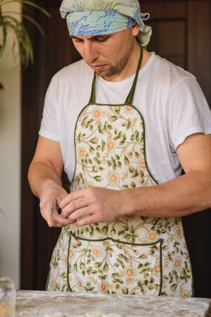 Handsome young man making small circles from raw dough, preparing potato dumplings, Traditional...