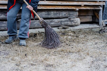 A woman in a village cleans a yard near her house with a birch broom. 2019の写真素材