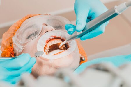 Dentist cleans teeth from stone using ultrasound, a woman sits in dental chair.2020