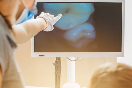 A young female dentist examines the teeth of a boy sitting in a dental chair with a dental...