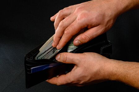 man removing dollars from his wallet, hands and wallet on black background.2020