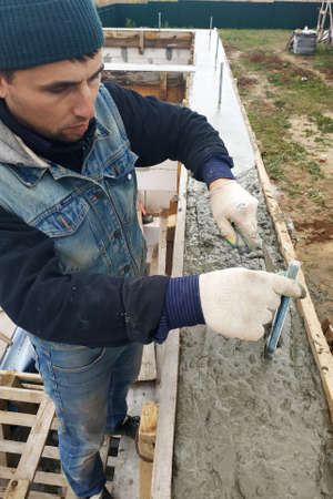 Worker lines concrete in formwork with trowel, construction of new home.2020